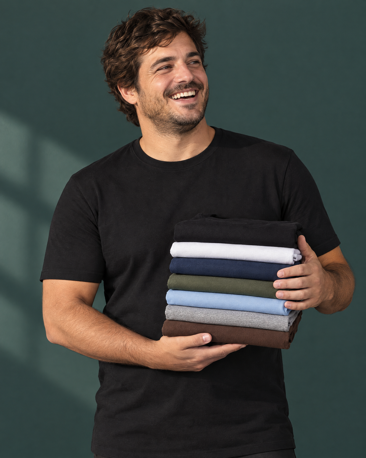 Hombre con remera Elemental negra sosteniendo remeras de 7 colores